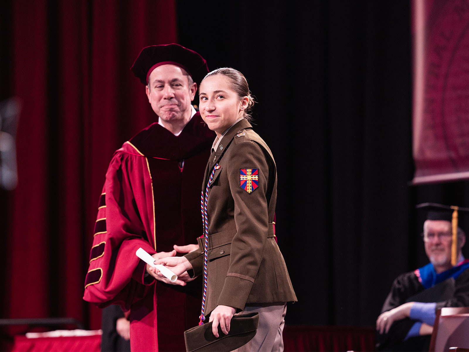 a woman in a uniform and a man in a robe shaking hands at CMU graduation
