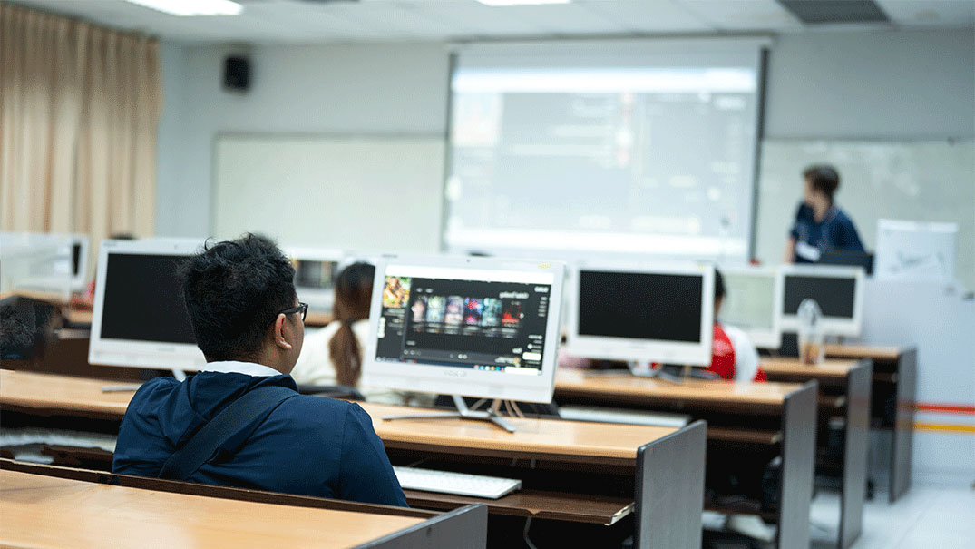 Lecturer teaching while students sit in front of a desktop