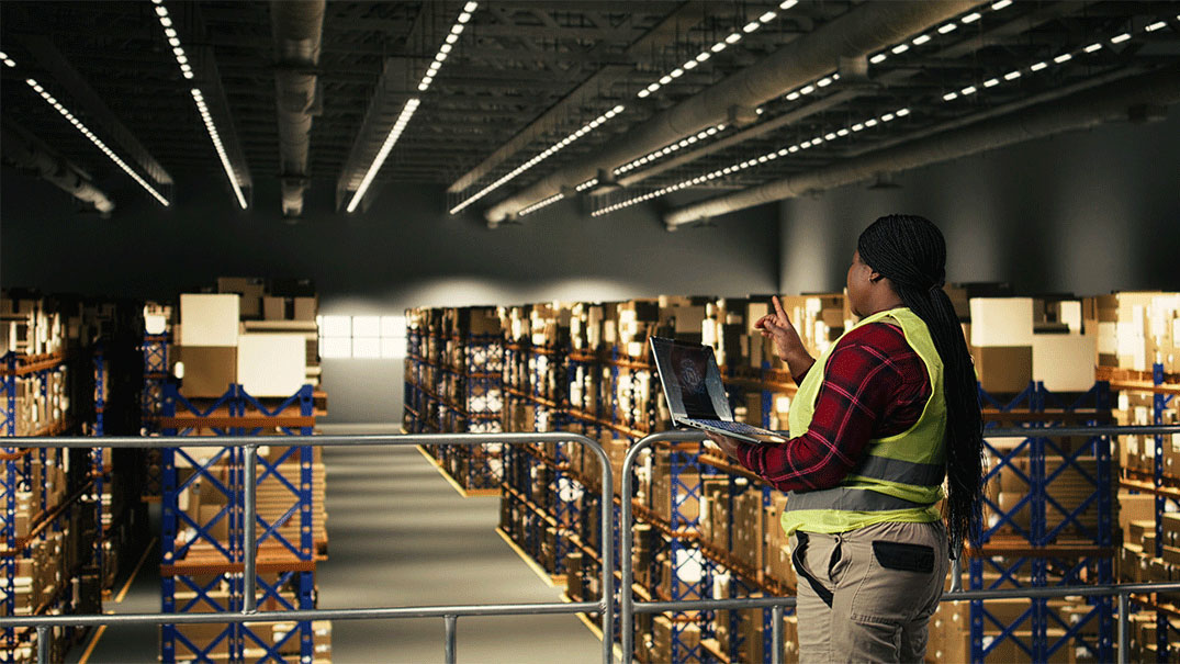 a woman in a safety vest holding a laptop in a warehouse
