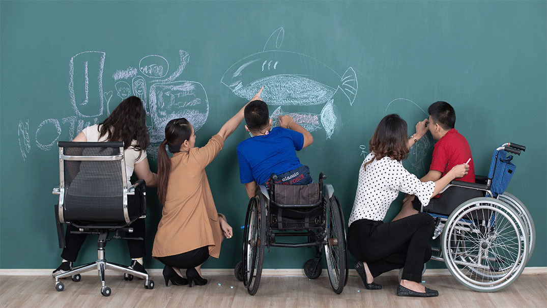 Two special education teachers with three students drawing on a blackboard