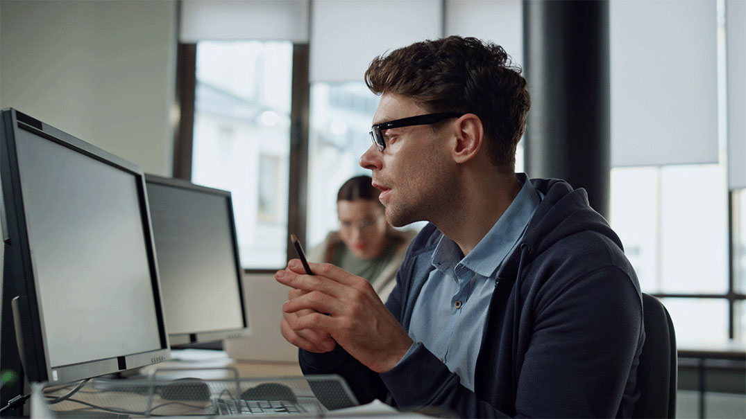 a man in glasses holding a pen reading something on a screen