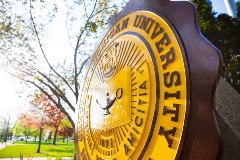 CMU's university seal, a large statue with our motto and a lamp of knowledge on it, is located in a tree-lined mall on campus.