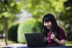 CMU Online student studies on her computer outdoors.