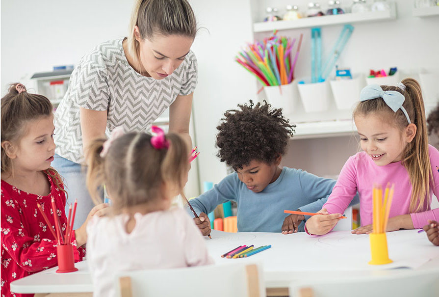 Teacher working with a group of young students in a bright open classroom.